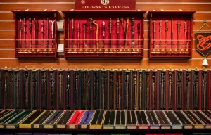 Présentoir mural de baguettes magiques Harry Potter de la collection Ollivander dans une boutique officielle, incluant la baguette de Sureau et celles des personnages principaux sur fond de velours rouge.