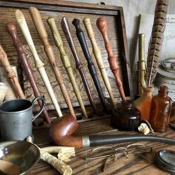 Collection de baguettes magiques en bois sculpté de différentes essences, disposées dans un coffret en bois avec des accessoires vintage comme une pipe, des lunettes et des flacons d'apothicaire.
