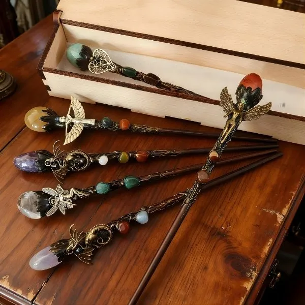 Collection de baguettes magiques artisanales ornées de pierres précieuses et cristaux dans un coffret de présentation en bois.