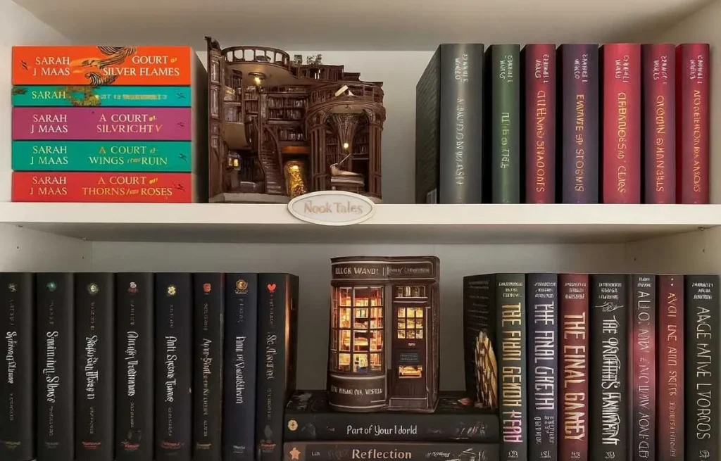Étagère de bibliothèque décorative avec des romans de Sarah J. Maas et des serre-livres lumineux miniatures de type "book nook" créant une ambiance magique.