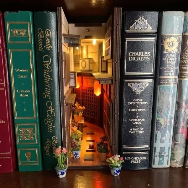 Décoration de bibliothèque Book Nook représentant une ruelle japonaise traditionnelle illuminée, insérée entre des livres classiques de Charles Dickens et Emily Brontë.