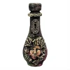 Petite bouteille décorative artisanale avec visage de femme sculpté dans des feuilles et serrure dorée ancienne sur fond de bois blanc.