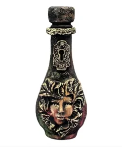 Petite bouteille décorative artisanale avec visage de femme sculpté dans des feuilles et serrure dorée ancienne sur fond de bois blanc.