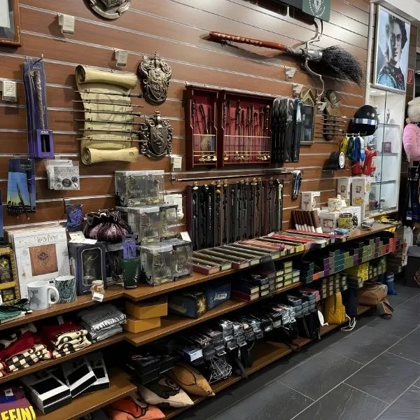 Rayonnage d'une boutique officielle Harry Potter présentant une large collection de baguettes magiques, le balai Nimbus 2000, des blasons de Poudlard et divers produits dérivés comme des mugs et des vêtements.