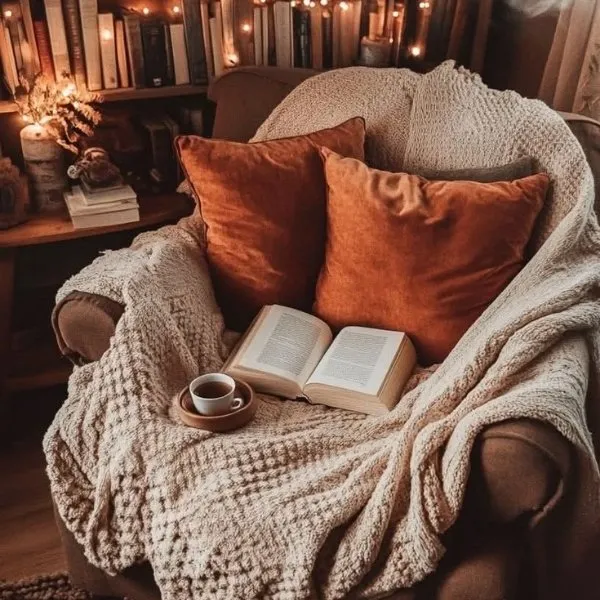 Livre ouvert et tasse de café sur un fauteuil avec couverture épaisse.