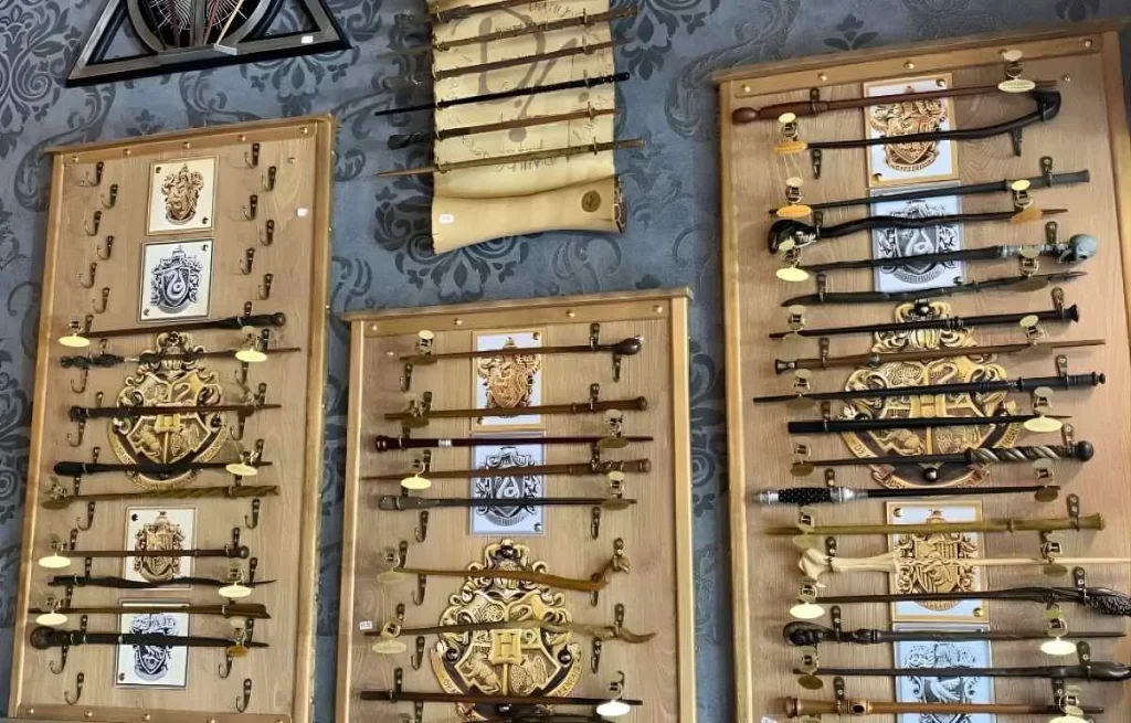 Exposition murale d'une collection de baguettes magiques Harry Potter présentées sur des supports en bois avec les blasons des maisons de Poudlard.