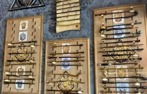Exposition murale d'une collection de baguettes magiques Harry Potter présentées sur des supports en bois avec les blasons des maisons de Poudlard.