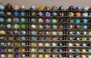 Étagère de présentation en bois exposant une vaste collection de dés à vingt faces (D20) artisanaux en résine aux couleurs et motifs variés