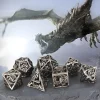 Set de 7 dés polyédriques de jeu de rôle en métal creux argenté avec motifs de dragons sculptés, présentés sur un rocher devant une illustration de dragon volant.