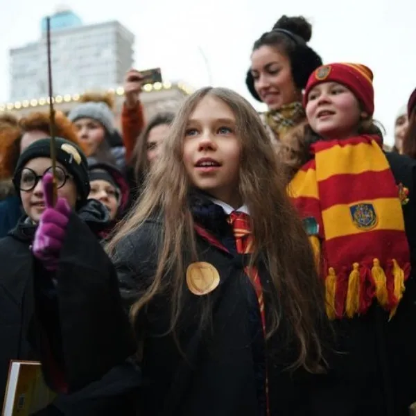Groupe de jeunes fans costumés en apprentis sorciers lors d'un événement au Warner Bros. Studio Tour, portant des écharpes rouge et jaune, des lunettes rondes et brandissant une baguette magique avec enthousiasme