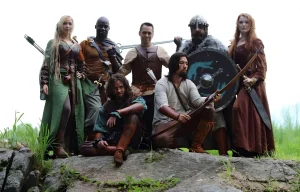 Un groupe de sept aventuriers en costumes médiévaux-fantastiques posant sur un rocher en extérieur, incluant des archers, des guerriers avec épées et boucliers, et une elfe