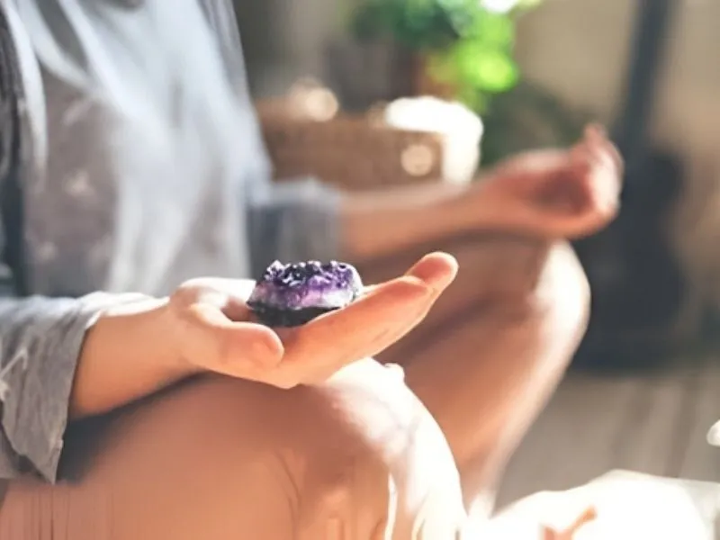 Femme en méditation tenant une géode d'améthyste pour favoriser la sérénité et la pleine conscience