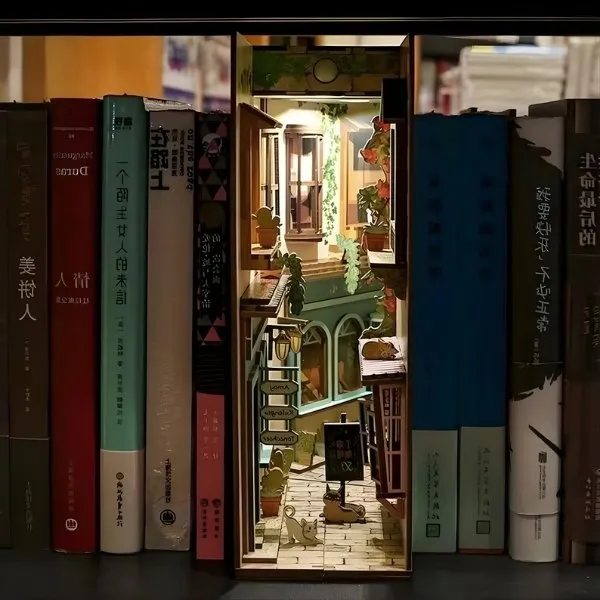 Insert de bibliothèque miniature représentant une ruelle verdoyante avec façades de magasins et plantes.