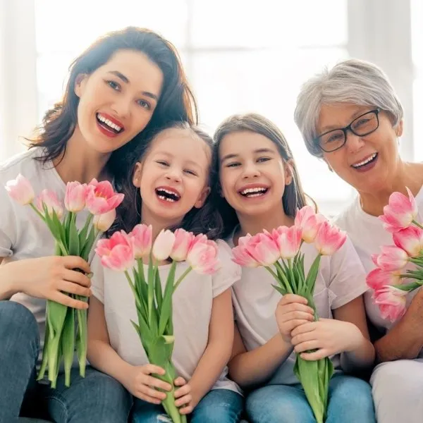 Trois générations de femmes souriantes tenant des bouquets de tulipes roses dans un intérieur lumineux