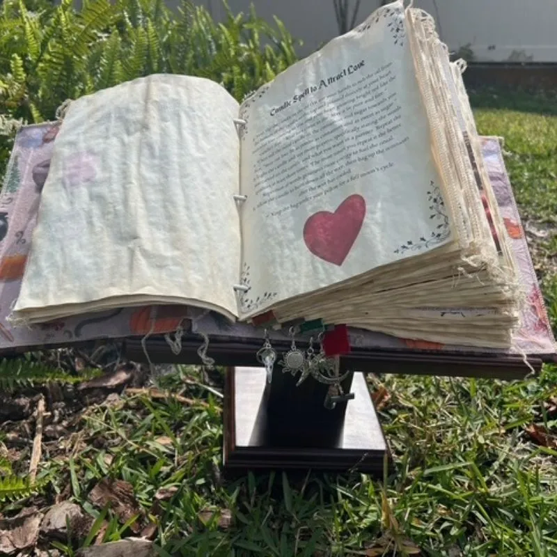 Livre des ombres ouvert dans l'herbe montrant des pages de parchemin usées avec un cœur rouge