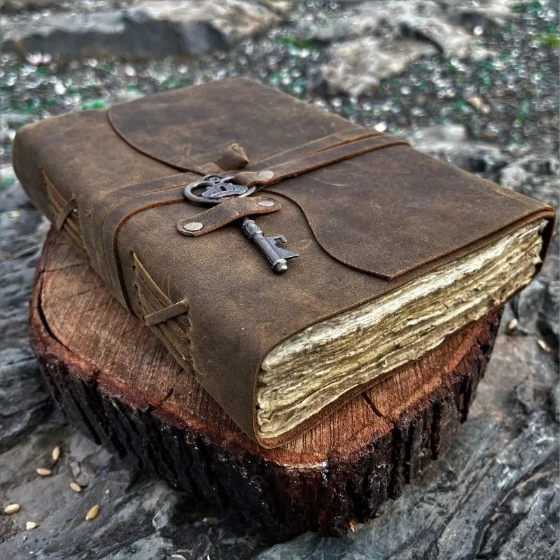 Grimoire en cuir véritable vieilli fermé par une lanière et une clé ancienne sur une souche de bois.