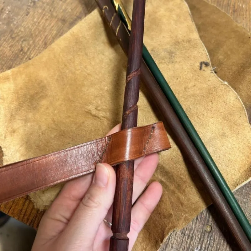 Gros plan sur les détails sculptés du manche d'une baguette magique en bois et son passant en cuir.