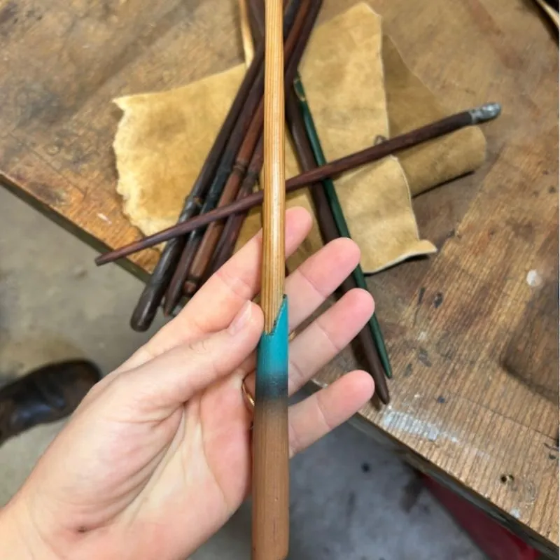 Baguettes magiques artisanales en bois noble posées sur un étui en cuir véritable dans un atelier.