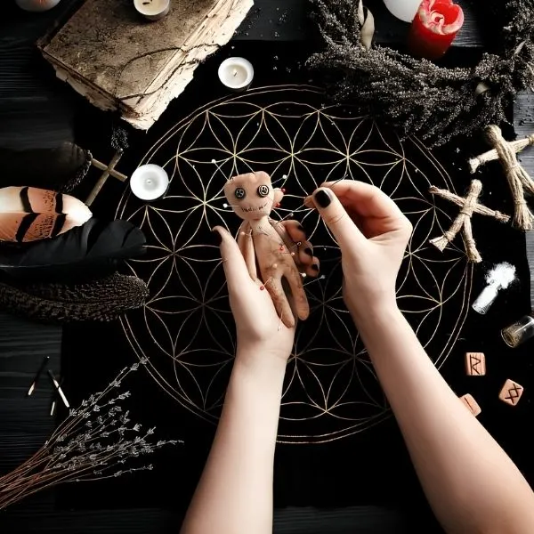 Mains d'une femme pratiquant un rituel de magie noire avec une poupée vaudou piquée d'épingles sur un autel ésotérique composé de runes, bougies et plumes.