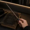 Baguette Lumineuse Ron tenue en main au-dessus d’un grimoire de magie
