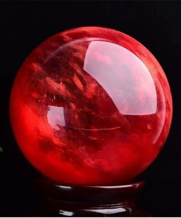 Boule de cristal écarlate en quartz naturel poli, rouge intense sur socle en bois.